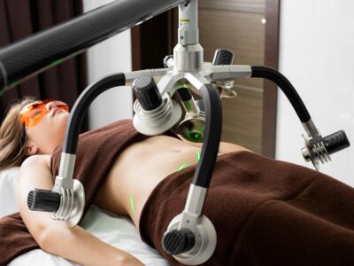 Cliente feminina deitada na mesa sob lasers de uma moderna máquina de perda de peso na barriga durante procedimento de lipoaspiração em clínica médica